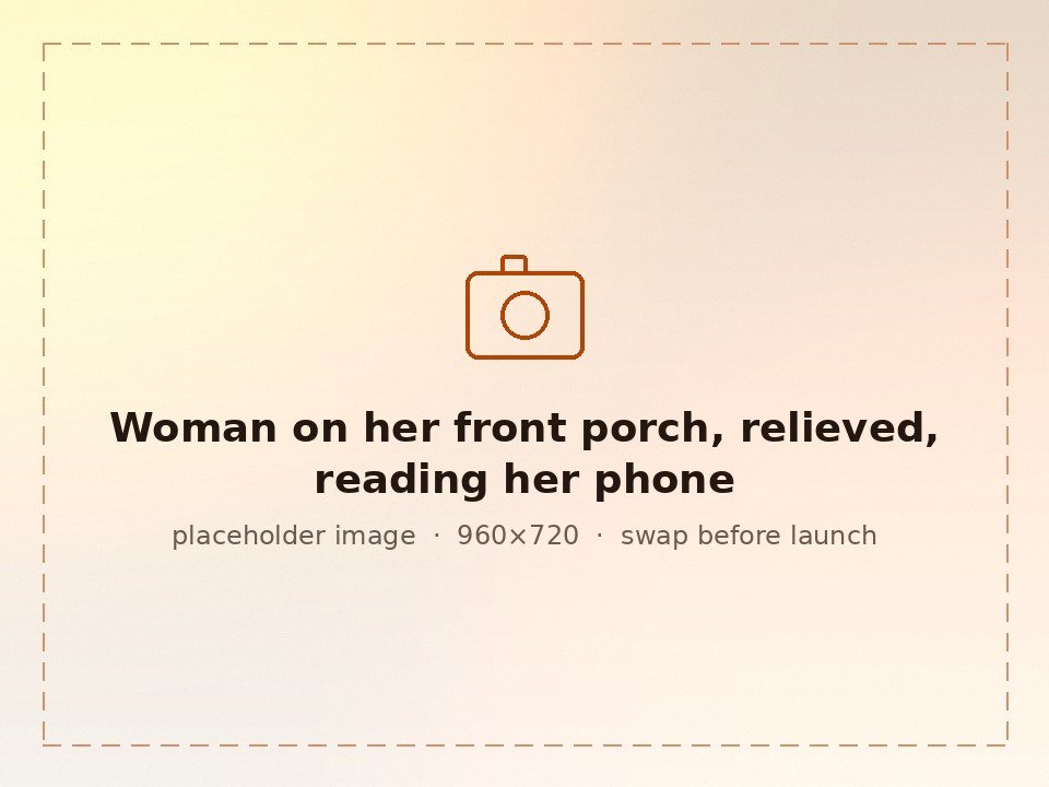 A woman on her front porch reading something on her phone with a relieved smile.